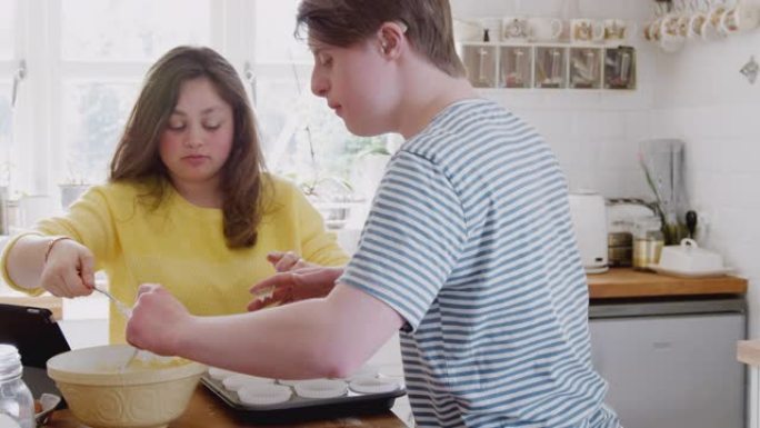年轻的唐斯综合症夫妇将混合物放入家里厨房的纸杯蛋糕盒中