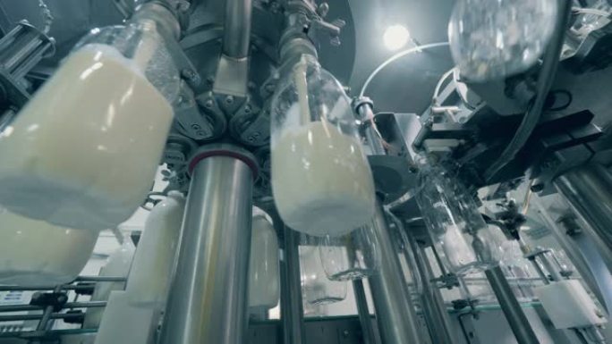 工厂机构正在用新鲜牛奶填充透明瓶子。装瓶厂设备。