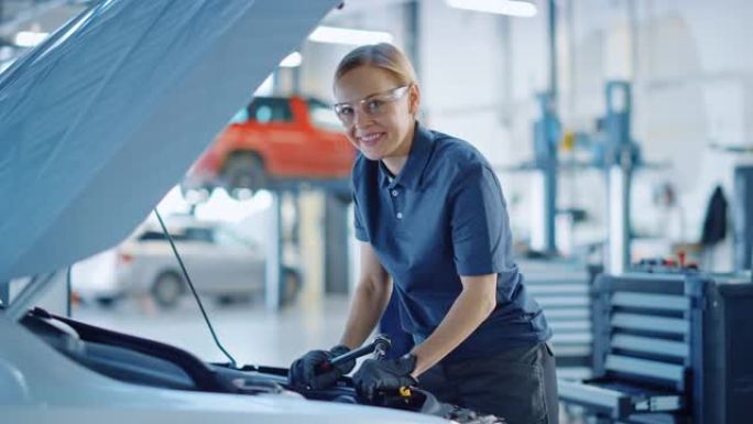 美丽的赋能女汽车修理工正在为服务中的车辆工作。她用棘轮时看起来很开心。专家戴着安全眼镜。她看着相机微