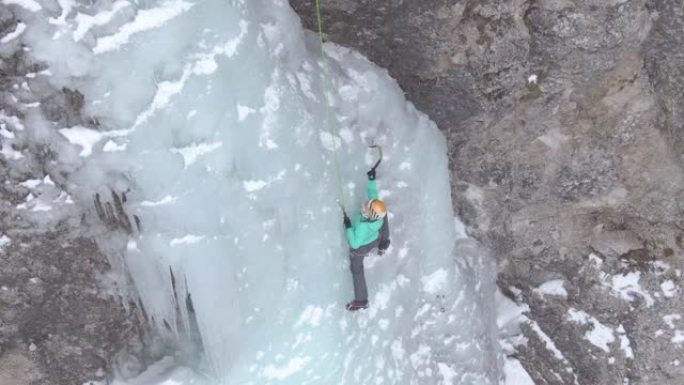 空中: 女人在爬上冰冷的瀑布时小心地放置冰镐