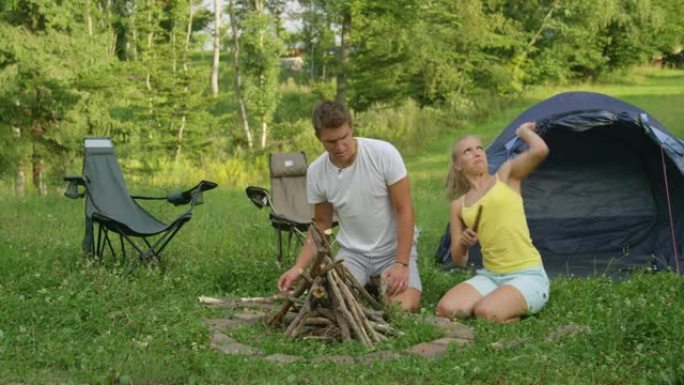 年轻女子在与男友准备篝火时试图驱赶昆虫。