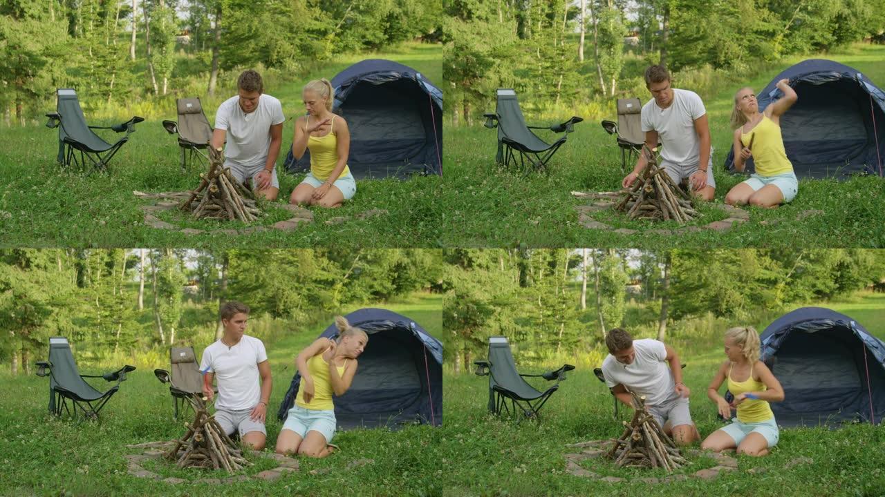 年轻女子在与男友准备篝火时试图驱赶昆虫。