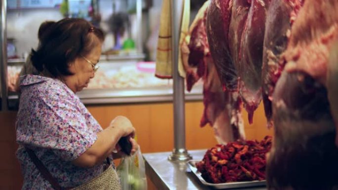 亚洲高级妇女在农贸市场购买肉类和猪肉