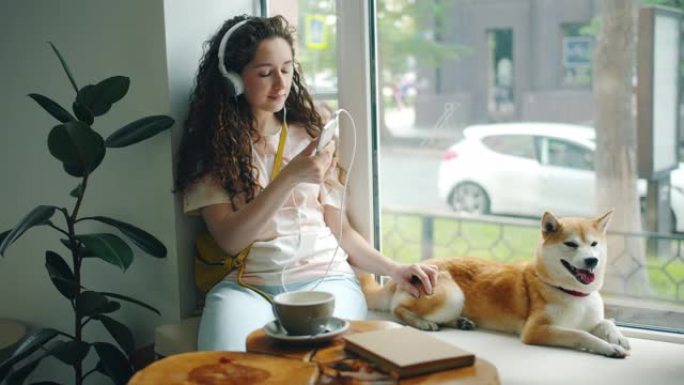 戴着耳机的女人在咖啡馆用智能手机抚摸宠物听音乐