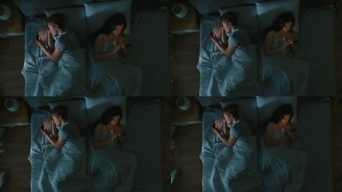 疏远的千禧一代年轻夫妇躺在床上，年轻人使用智能手机互相远离，浏览社交网络，不互相交谈。自上而下的相机