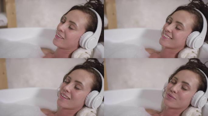 放松的女人在浴缸里戴着耳机听音乐