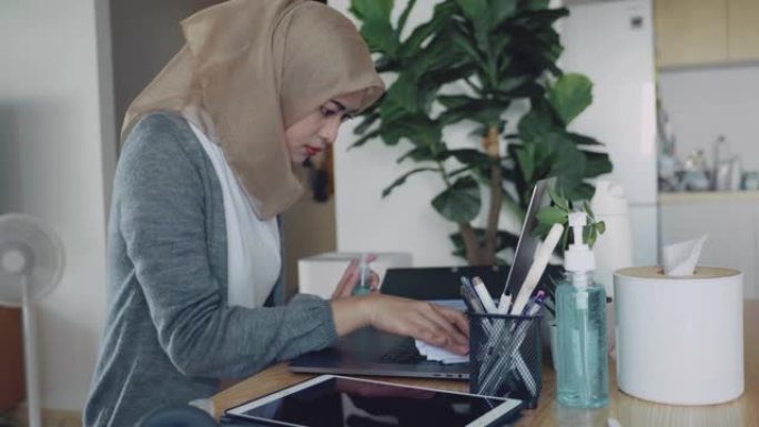 穆斯林妇女在家清洁笔记本电脑和数字平板电脑。