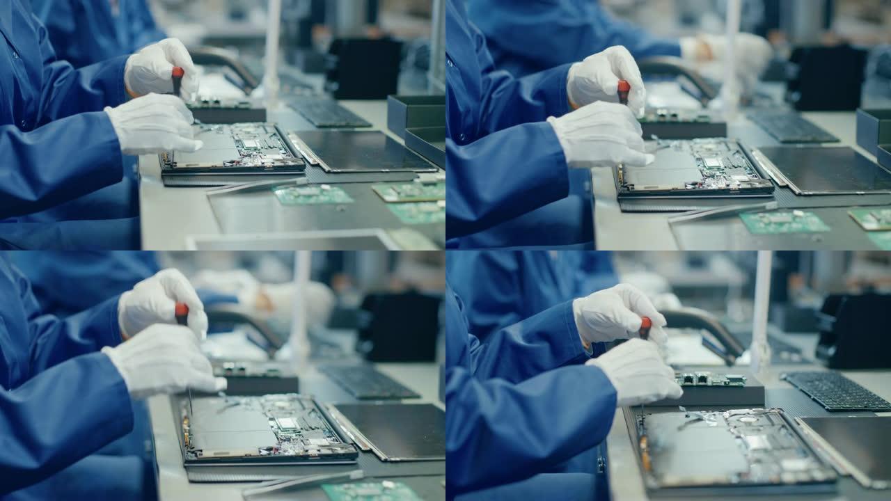 一名穿着蓝色工作服的电子工厂女工人的特写镜头，用螺丝刀组装笔记本电脑的主板。拥有多名员工的高科技工厂