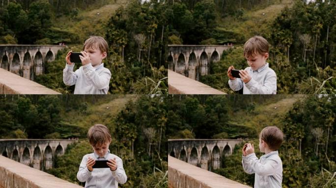 斯里兰卡度假时，快乐可爱的欧洲小男孩在埃拉九拱桥拍摄智能手机照片。