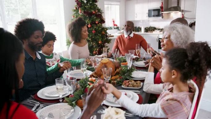 多代混血家庭坐在圣诞节的桌子上，手牵着手说恩典，选择性聚焦，高高的视野