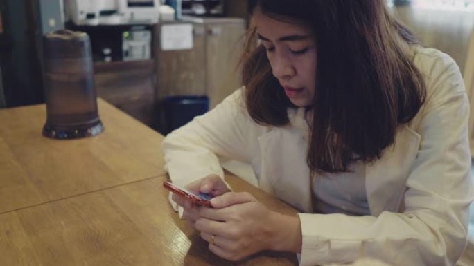 年轻女子坐在智能手机上聊天，坐在餐厅里。