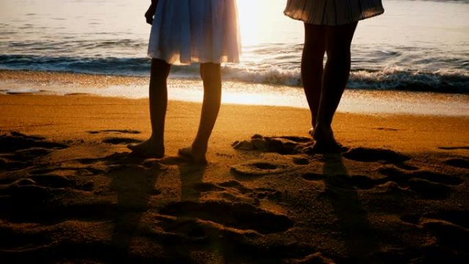 年轻的母亲和小女儿手牵手，在令人难以置信的海滩观看史诗般的日落的惊人后景拍摄。