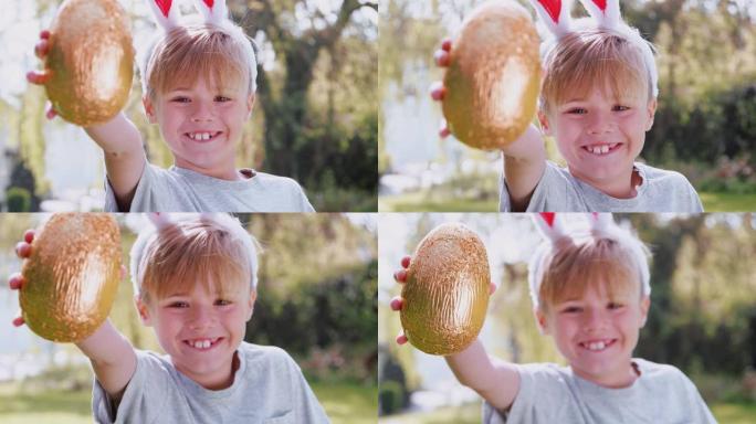 男孩在家里的复活节彩蛋狩猎中戴着兔子耳朵的肖像举着巧克力蛋对着镜头，微笑着慢动作拍摄