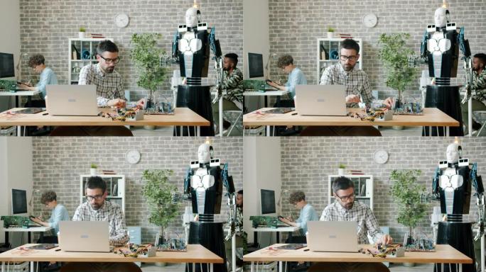 多民族创意团队使用计算机在办公室设计机器人。人、团队精神和现代科技理念。