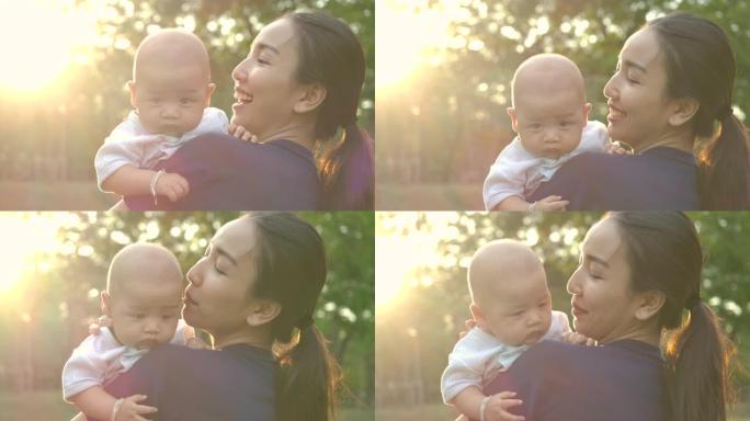 妈妈在公园和婴儿玩耍。年轻的亚洲母亲带着幸福的情感在公园或花园高高举起她的宝贝儿子。慢动作。