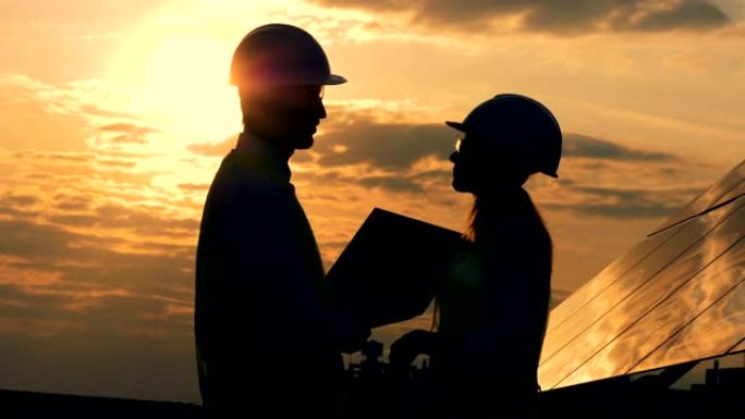 男人和女人建筑工人在日落背景下交谈，侧视图。