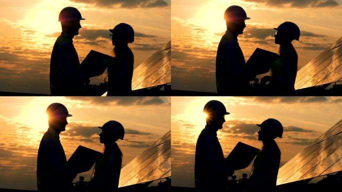 男人和女人建筑工人在日落背景下交谈，侧视图。