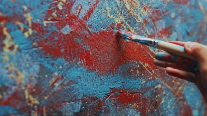 女艺术家手的特写镜头，拿着画笔，用红色颜料画画。色彩缤纷，富有情感的油画。当代画家创作现代抽象美术作