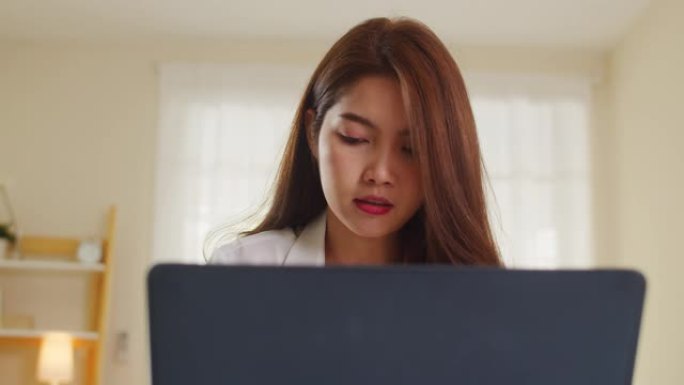 自由职业亚洲女性的肖像，穿休闲装使用笔记本电脑在家里的客厅工作。