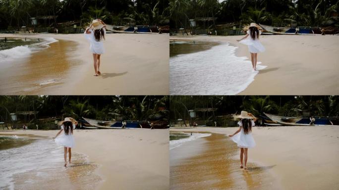 镜头跟随快乐兴奋的5-7岁小女孩戴着大草帽沿着异国情调的热带海洋海滩散步。