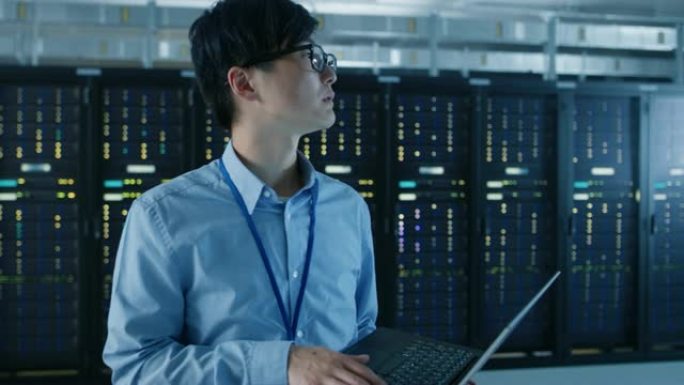 在现代数据中心: IT工程师的肖像站在他身后的服务器机架上，使用笔记本电脑进行维护和诊断程序。弧形摄