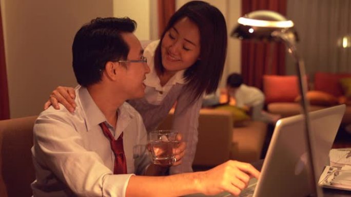 微笑的妻子用笔记本电脑在家照顾丈夫。
