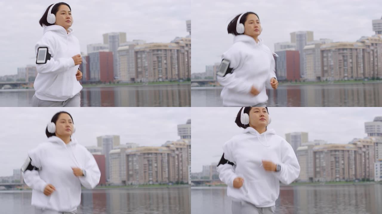戴着耳机的亚洲女性在城市河边慢跑