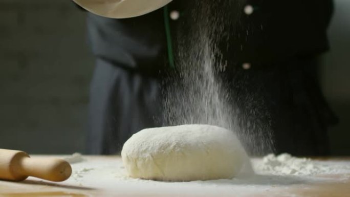 无法辨认的面包师在面团上筛分面粉