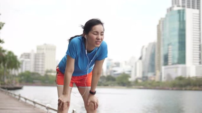 亚洲女子跑步累了，在城市里看着她的智能手表