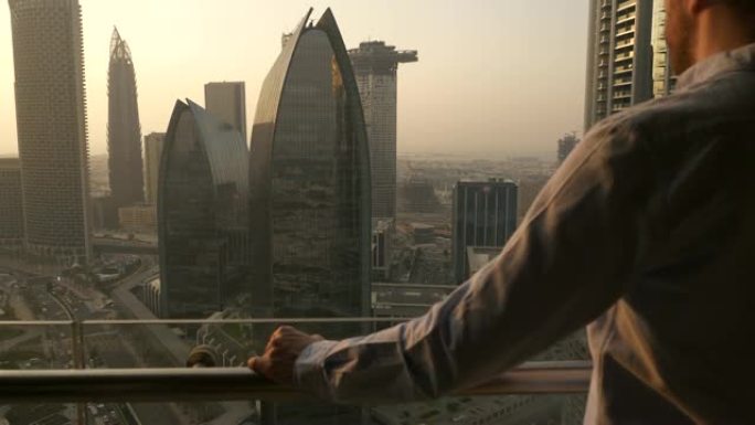 年轻的白人男子站在阳台上看着摩天大楼的现代城市
