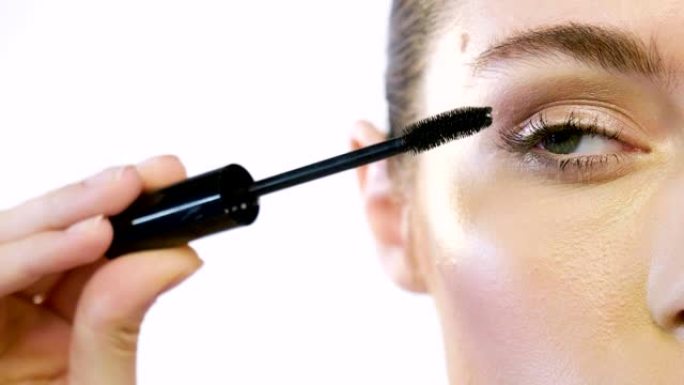女人将睫毛膏涂在眼睛上，以制作最佳妆容，并突出眼睛的颜色和特征。