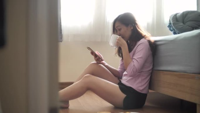 亚洲女性在卧室使用带咖啡杯和早餐的智能手机
