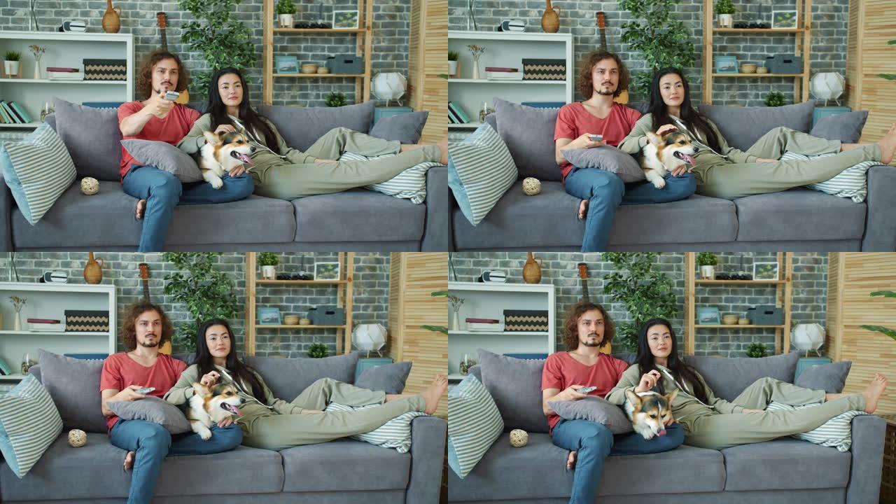 年轻人夫妇与威尔士柯基狗狗在家里看电视电影