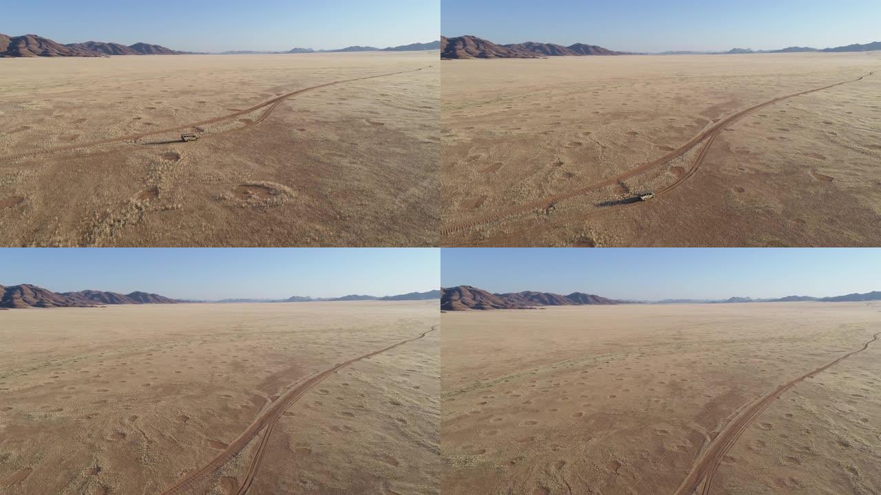 4k高倾斜鸟瞰图，一辆4x4野生动物园车辆在沙路上行驶，穿过非洲大草原，与著名的仙女圈，纳米比亚