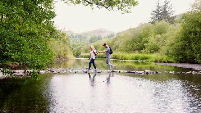 年轻夫妇在英国湖区徒步旅行时使用垫脚石过河的慢动作镜头