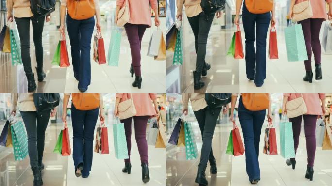低镜头的女性购物者一起走在购物中心，拿着礼品袋和购物享受销售。人、消费主义和购物狂概念。
