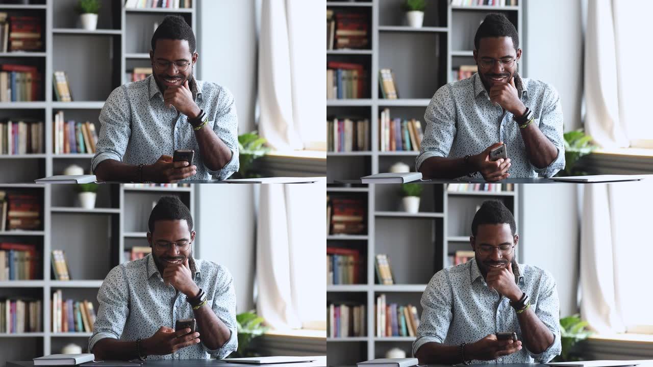 快乐的年轻成年非洲男子在家庭办公室使用智能手机