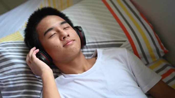 周末躺在床上的一个亚洲华裔少年男孩在家用耳机听音乐