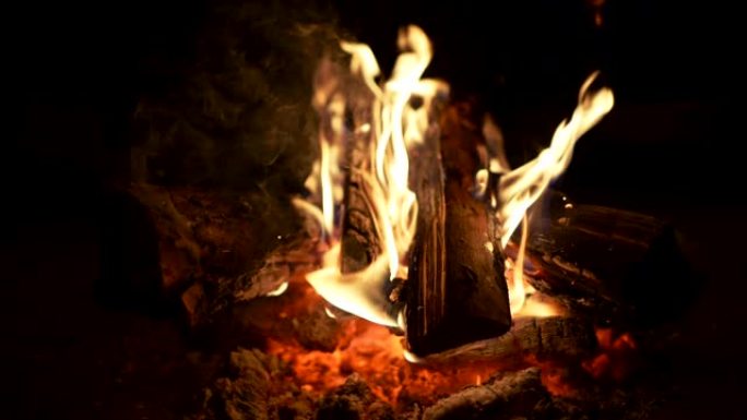 在户外的傍晚篝火中，燃烧的原木被火焰吞没。慢动作镜头