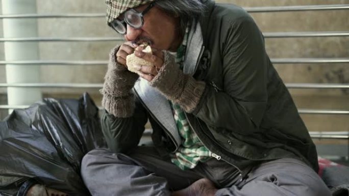 向上倾斜: 无家可归的人吃食物并坐在人行道上。