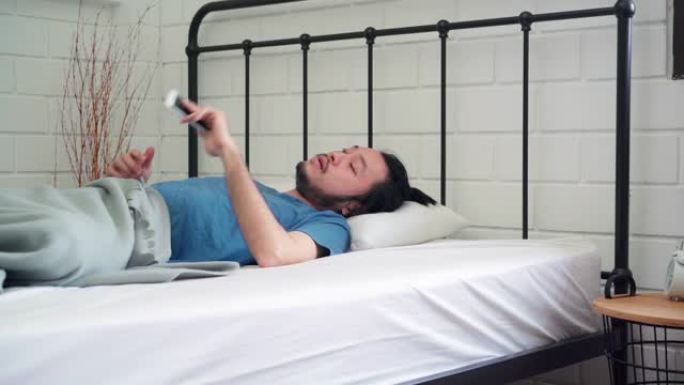年轻的亚洲男子早上醒来，亚洲男子用手机查看社交媒体，醒来后在卧室的床上发送信息。英俊的男人午睡，困在