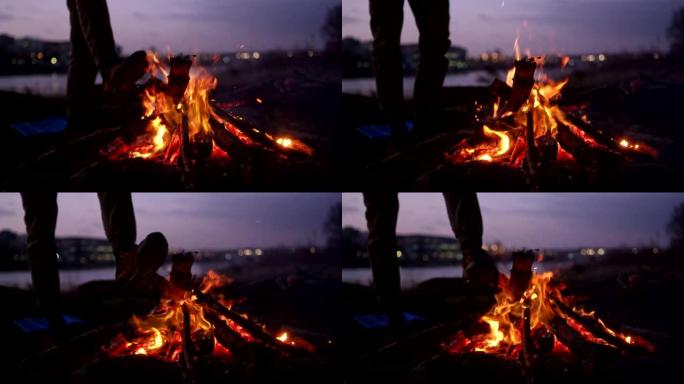 孤独的人在河边燃烧篝火。预热脚