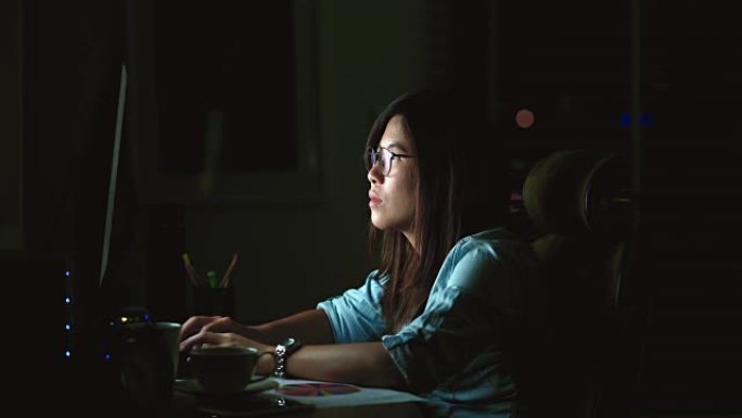 4k镜头有吸引力的亚洲女性工作到很晚，在黑暗中工作场所的计算机显示器桌面前的桌子上认真行动，工作到很