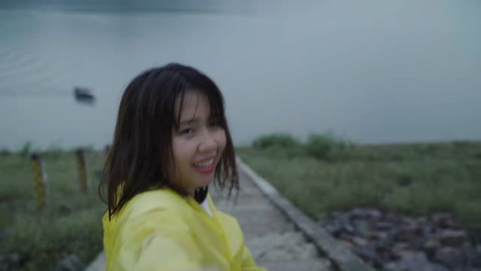 慢动作 -- 年轻的亚洲女人穿着雨衣站在湖边玩雨感到快乐。生活方式女性在雨天享受和放松。