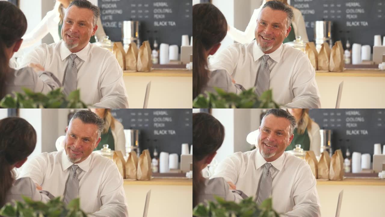 一个穿着正装衬衫和领带的成熟成年男子，坐在咖啡店里时，与他对面的一个女孩握手。