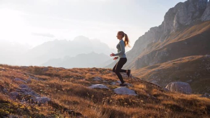 健康的女运动员保持健康的生活方式，在日落时分在多岩石的小径和草坡上奔跑