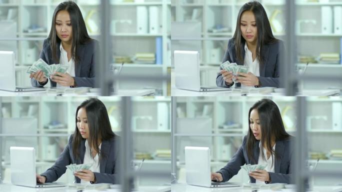 亚洲女会计师数美元和在笔记本电脑上工作