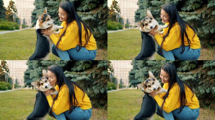在城市公园户外拥抱和亲吻柯基狗的亚洲女孩的慢动作