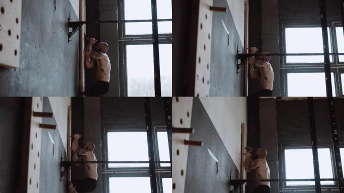 运动年轻的赤裸上身的高加索运动员在健身房进行极限体育锻炼时爬上巨石健身房的墙壁。