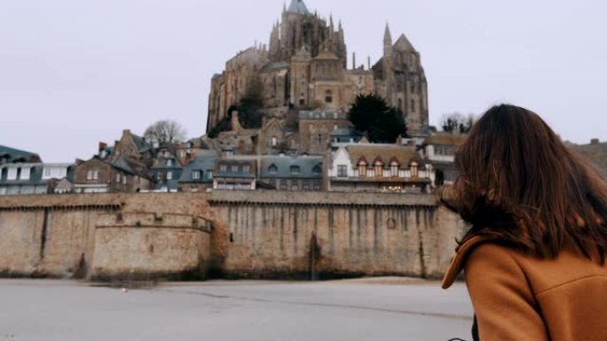 时尚博主女人走向法国令人惊叹的圣米歇尔山城堡地标慢动作的电影后视